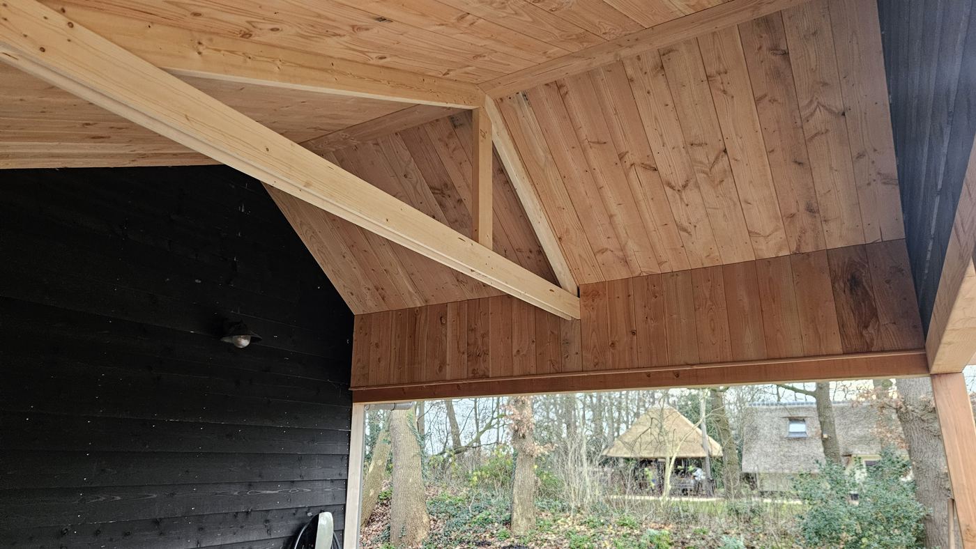 Plafond van houten rabatdelen onder het dak van de carport, met zichtbare balken en schoren