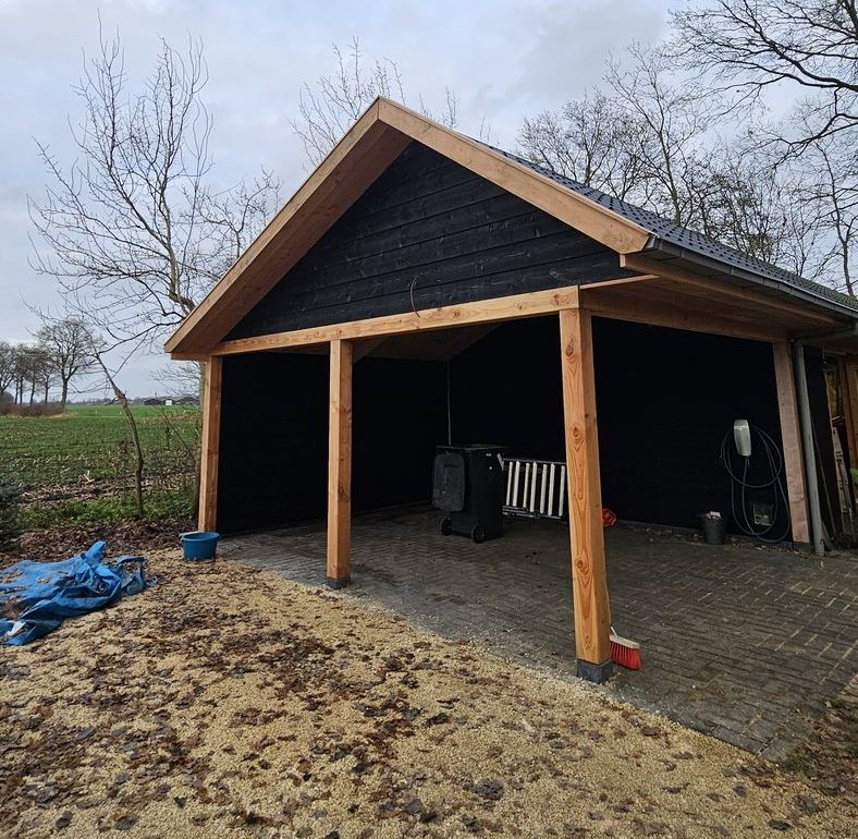 Open carport met staanders en randbalken van douglas, zwarte houten gevelbekleding en een donker pannendak