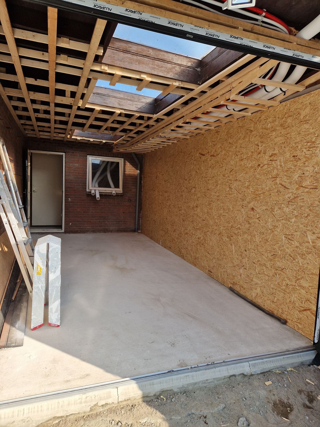 Binnenkant van de verbouwde berging met nieuwe betonvloer, wand van OSB-platen en een raster van latten tegen het plafond