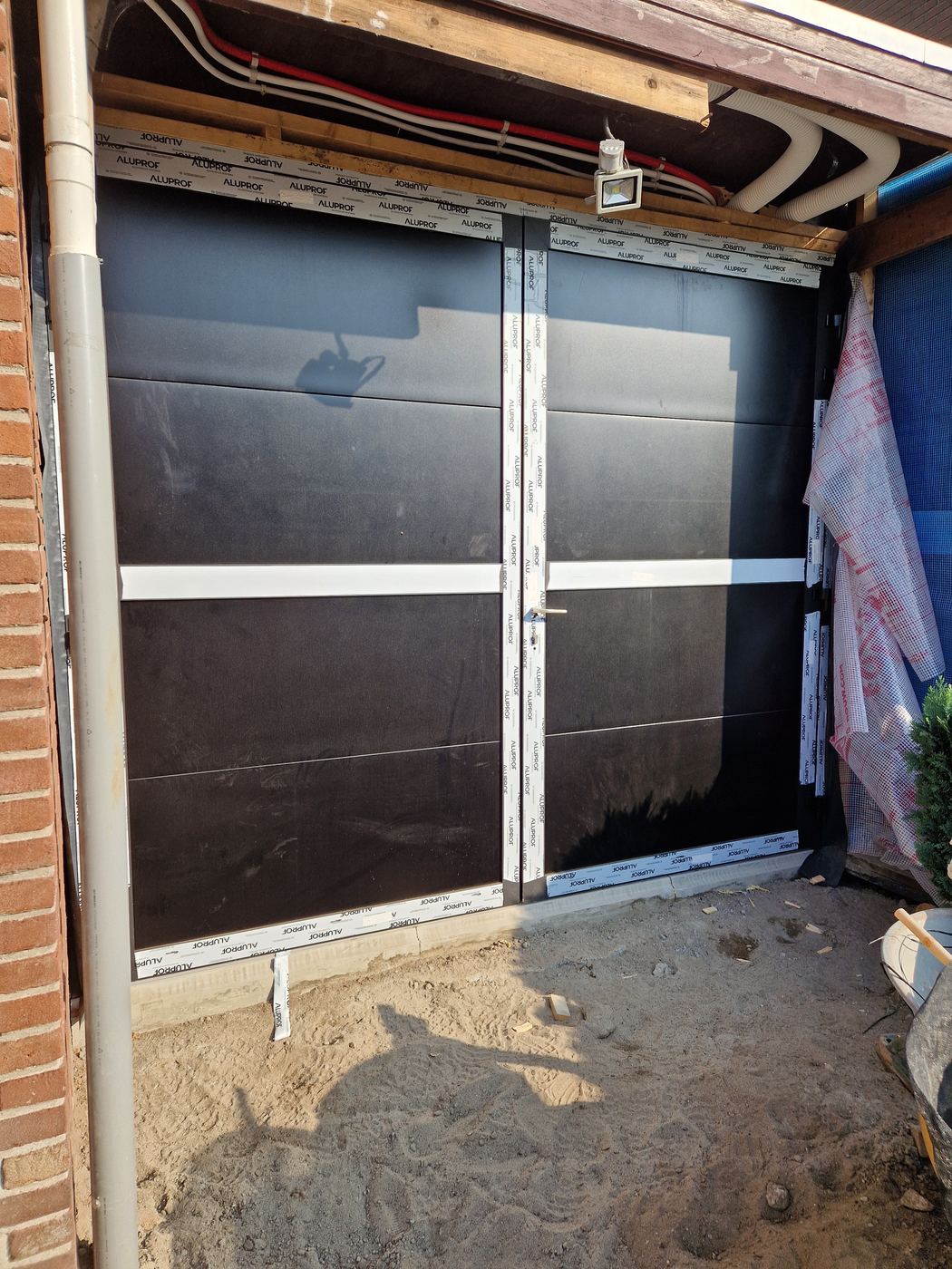Nieuwe dubbele zwarte deuren in de gevel, nog met beschermfolie op de kozijnen